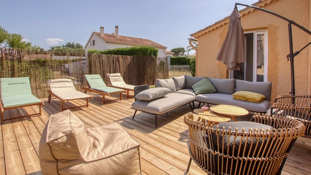 Une terrasse en bois avec des chaises longues, un canapé et un fauteuil en osier.