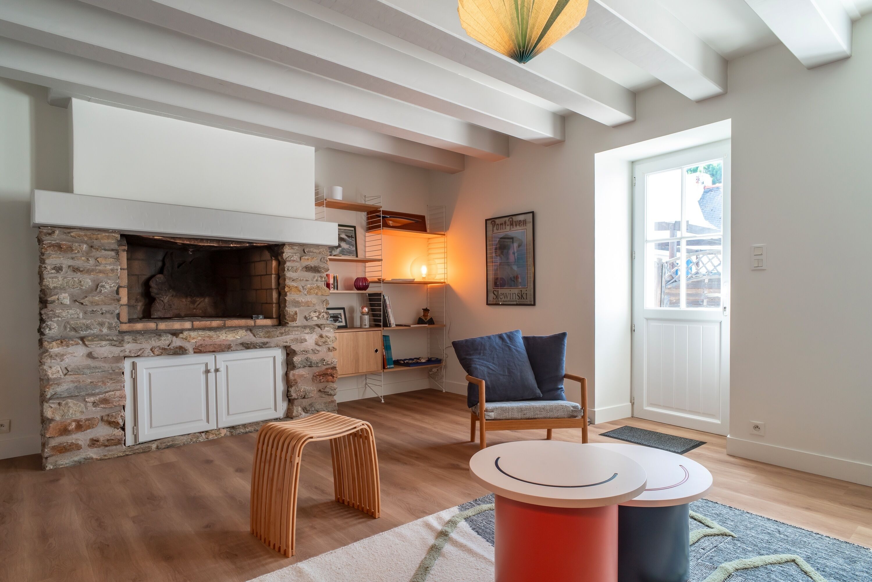 A cozy living room with a stone fireplace, wooden furniture, and a view of the outdoors.