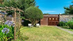 A garden with a wooden pergola, two white benches, a stone wall, and a wooden gate.