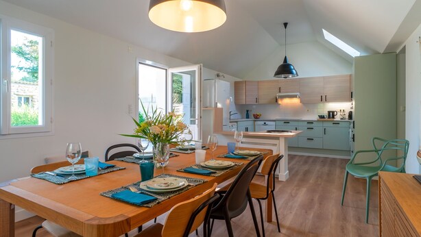 A modern kitchen with wooden cabinets, a dining area with a wooden table set for four, and a skylight above.