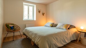 A bedroom with a large bed, a window, a chair, and a bedside table with a lamp.