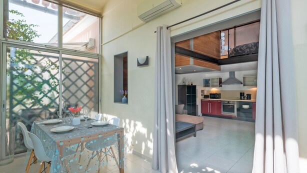 A dining area with a table set for four, a kitchen in the background, and a sliding door leading to another room. - Le Scarlett - Maison à 300m de la plage (Palavas-les-Flots)