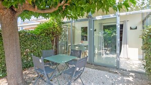 A patio with a table and chairs, surrounded by a tree and a hedge. - Le Scarlett - Maison à 300m de la plage (Palavas-les-Flots)