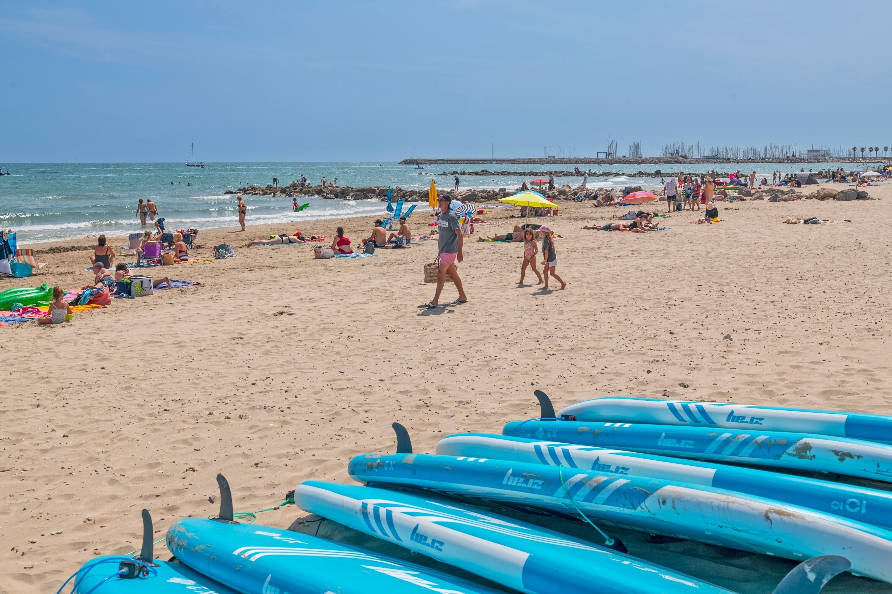 A beach with people relaxing, umbrellas, and surfboards.