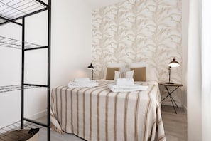 Een keurig opgemaakt slaapkamer met een bed, twee bedlampen, een klein nachtkastje en een metalen rek.