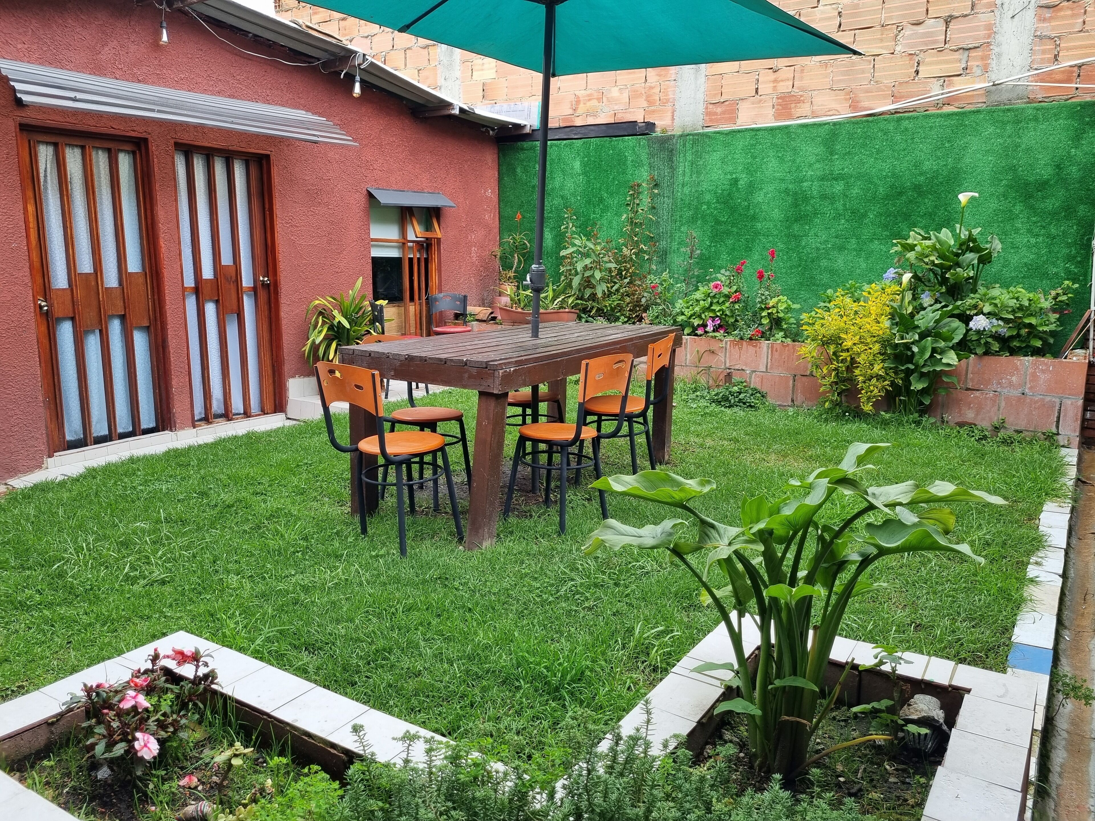 A patio with a wooden table and chairs, surrounded by a well-maintained lawn and various potted plants.