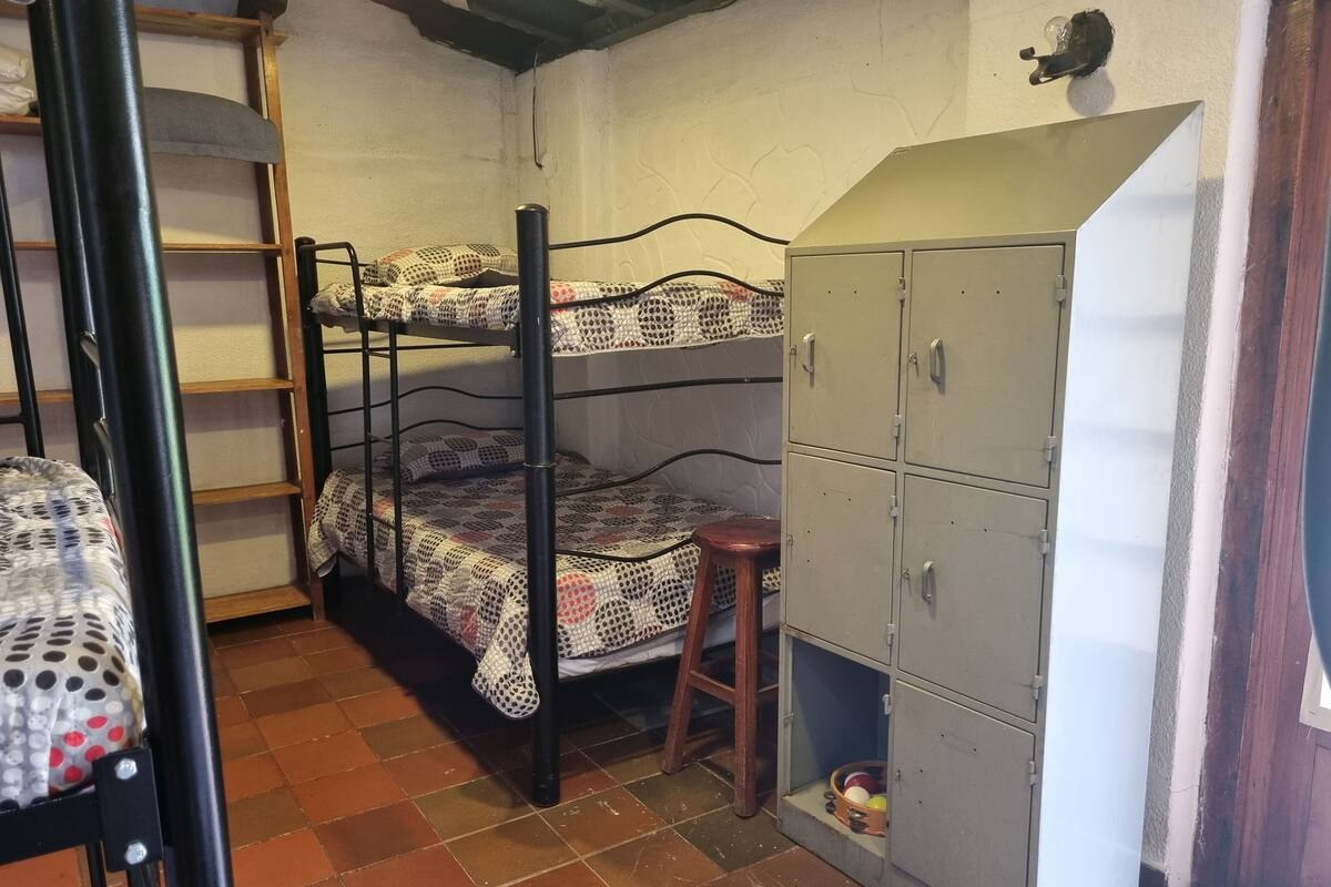 Um quarto em dormitório com beliches, um banquinho e um guarda-roupa.