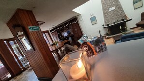 Um hall de hotel com uma recepção de madeira, uma área de estar com um sofá azul, uma lareira e uma televisão fixada na parede.