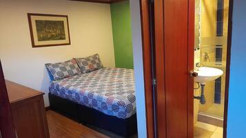 Un dormitorio con cama, armario de madera, pared verde y baño con lavamanos y espejo.