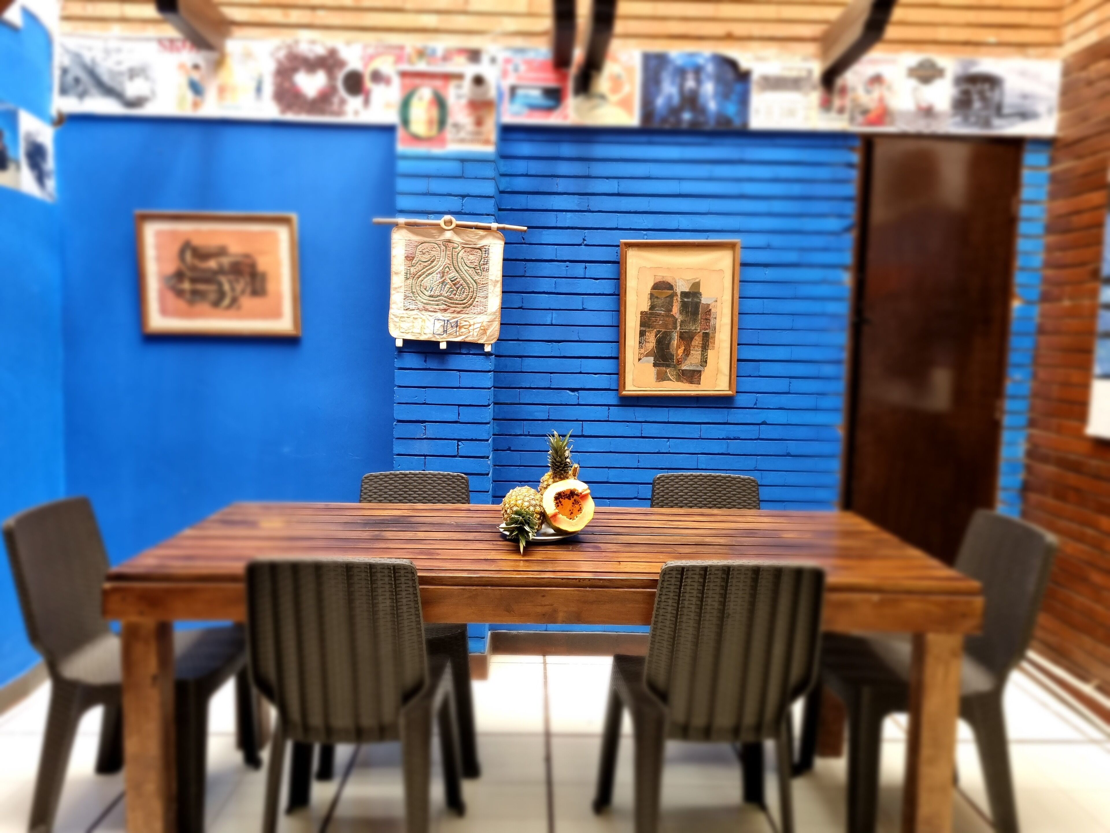 A dining area with a wooden table and four chairs, blue brick walls, and framed artwork.