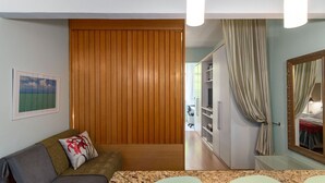 Una habitación con un separador de madera, un sofá con un cojín estampado, un cuadro en la pared y un espejo con cortina.