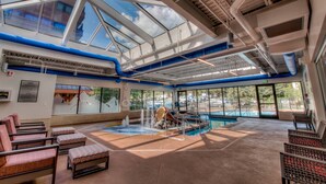 A spacious indoor pool area with clear views of the outside, a water slide, and seating areas.