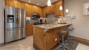 A modern kitchen with wooden cabinets, stainless steel appliances, a granite countertop, and pendant lighting.