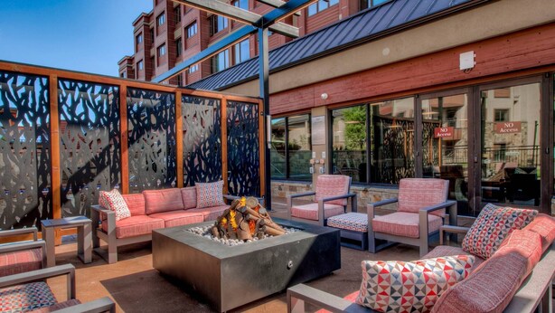 An outdoor seating area with sofas and chairs, a fire pit, and a view of a building with barred windows.