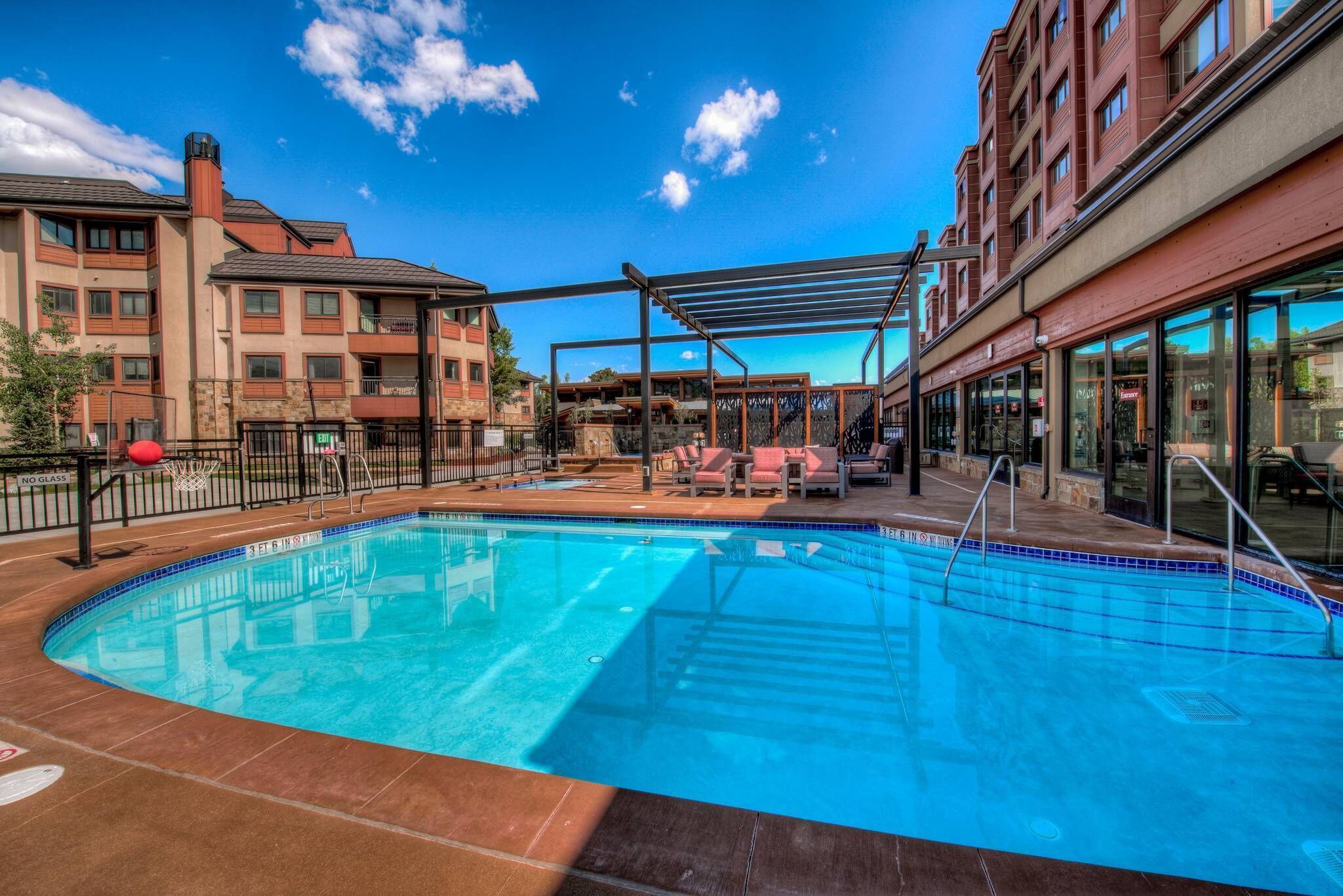 A swimming pool with a pergola and lounge chairs, surrounded by multi-story buildings with balconies.