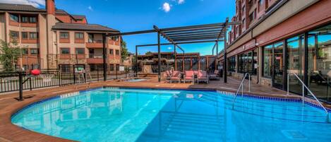 A swimming pool with a pergola and lounge chairs, surrounded by multi-story buildings with balconies.