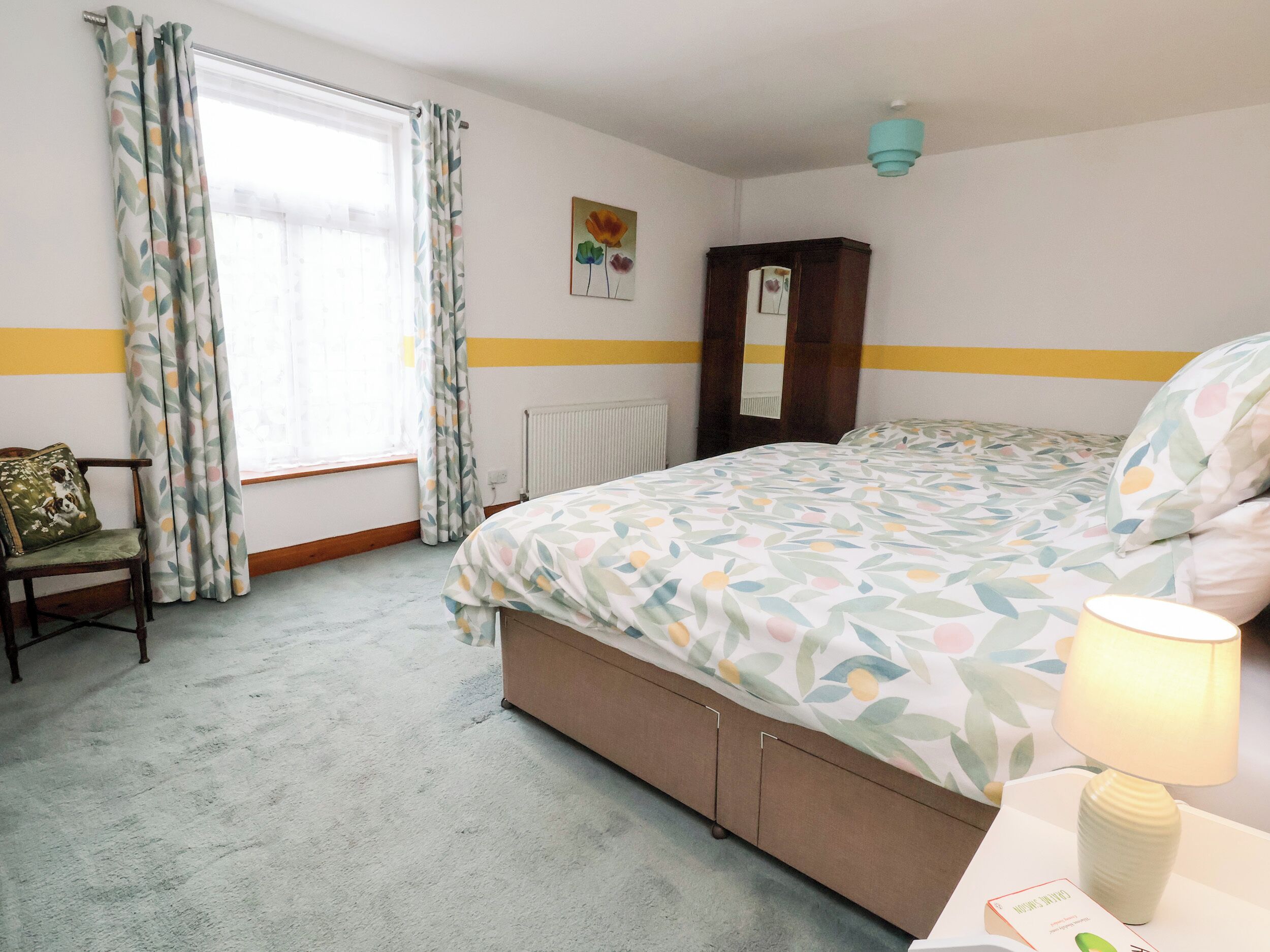 Un dormitorio con cama, una silla, una lámpara y un ventanal con cortinas.