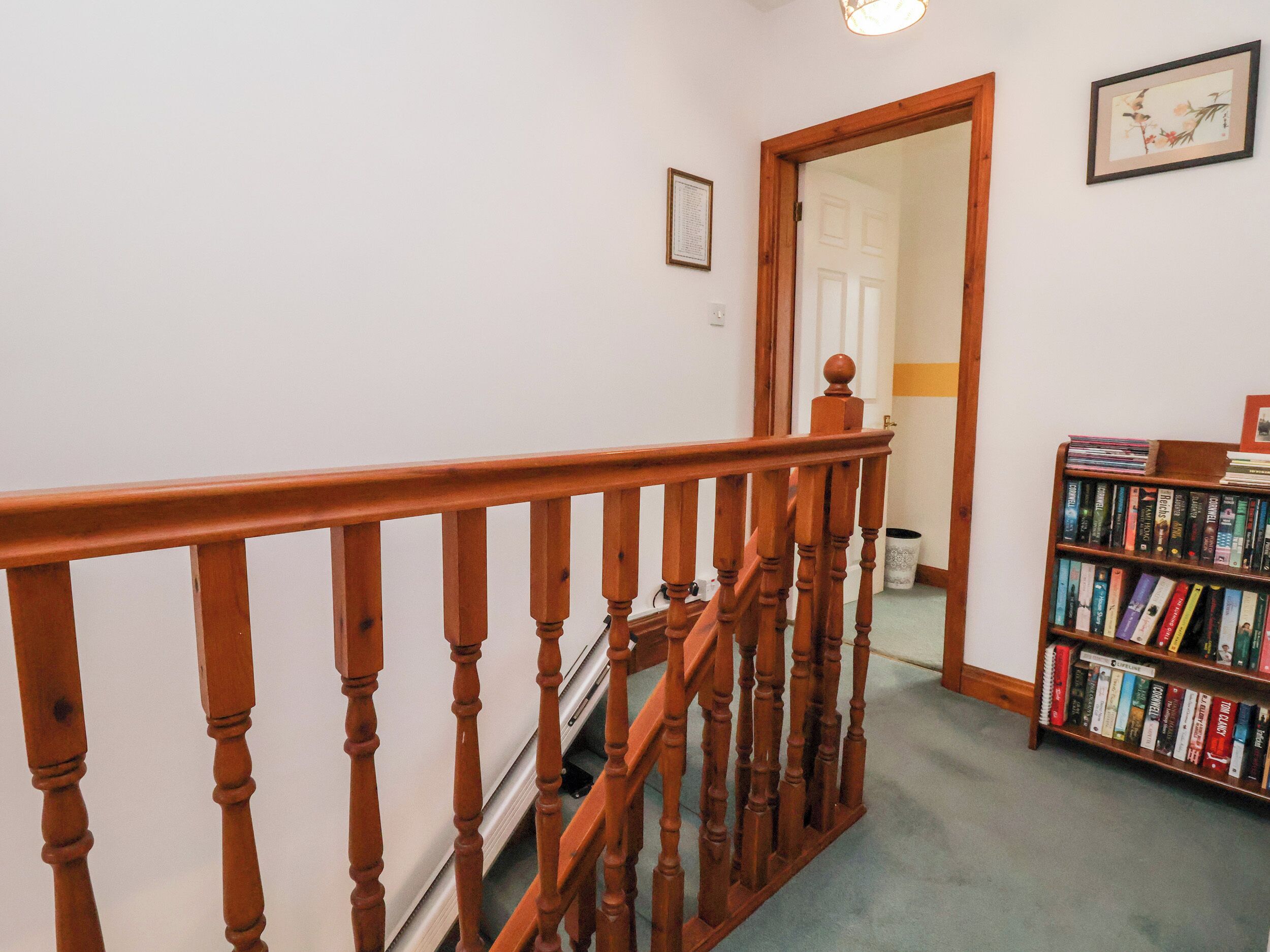 Una escalera de madera con barandilla que conduce a una puerta. A la derecha se ve una estantería llena de libros.