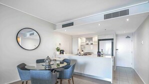Une cuisine moderne avec un îlot central, un coin repas avec une table ronde et des chaises, et un grand miroir au mur.