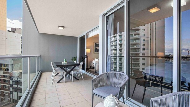 Un balcon équipé d’une table à manger, de chaises et d’un coin salon comprenant un fauteuil rembourré et un objet décoratif.
