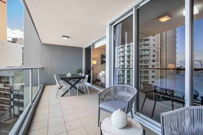 A balcony with a dining table, chairs, and a seating area with a cushioned chair and a decorative item. - Holly's City Skyline-Views, Pool, Spa, CBD Central (Brisbane)