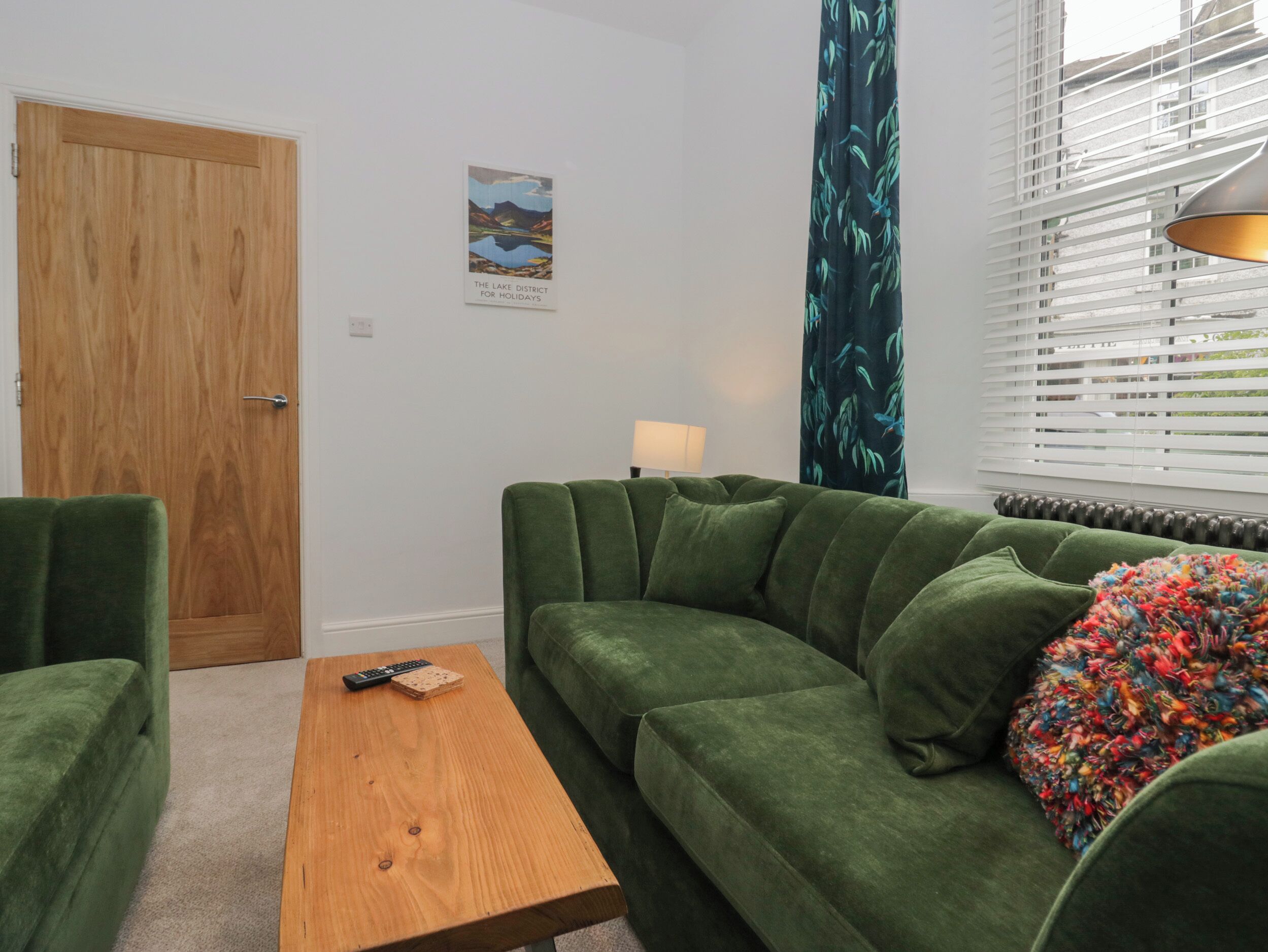 A green sofa, a wooden coffee table, and a lamp in a room with a wooden door and a poster on the wall.