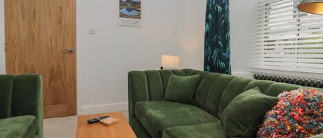 A green sofa, a wooden coffee table, and a lamp in a room with a wooden door and a poster on the wall.