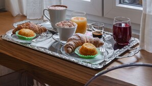 Una bandeja de desayuno con cruasanes, muffins, café y jugo, sobre una mesa de madera cerca de una ventana con cortinas.