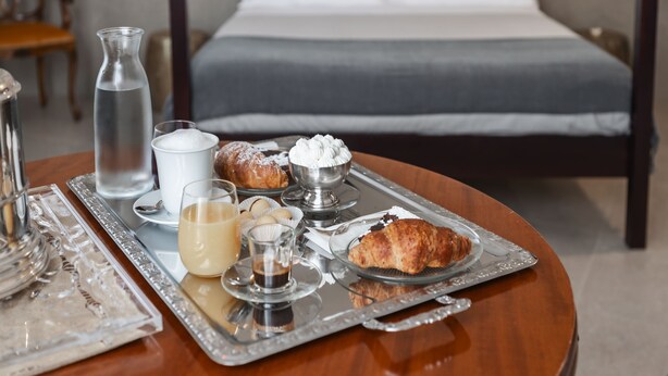 Una bandeja de desayuno bien dispuesta con pasteles, un croissant y un vaso de leche sobre una mesa de madera en una habitación de hotel.