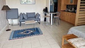 A compact living space with a sofa, a small table, a kitchen area, and a bed.