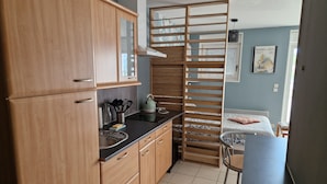A compact kitchen with wooden cabinets, a black countertop, and a small dining area with a chair.