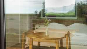 Un dormitorio con una cama, una mesa de madera con un jarrón de flores y una ventana con vistas a un paisaje.