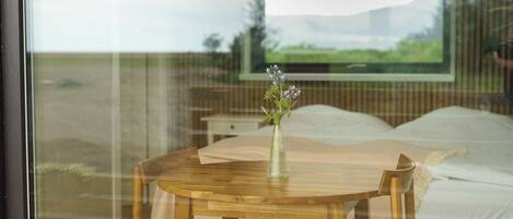 Un dormitorio con una cama, una mesa de madera con un jarrón de flores y una ventana con vistas a un paisaje.