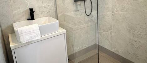 A modern bathroom with a glass-enclosed shower, a white vanity with a mirror, and a towel hanging on the wall.