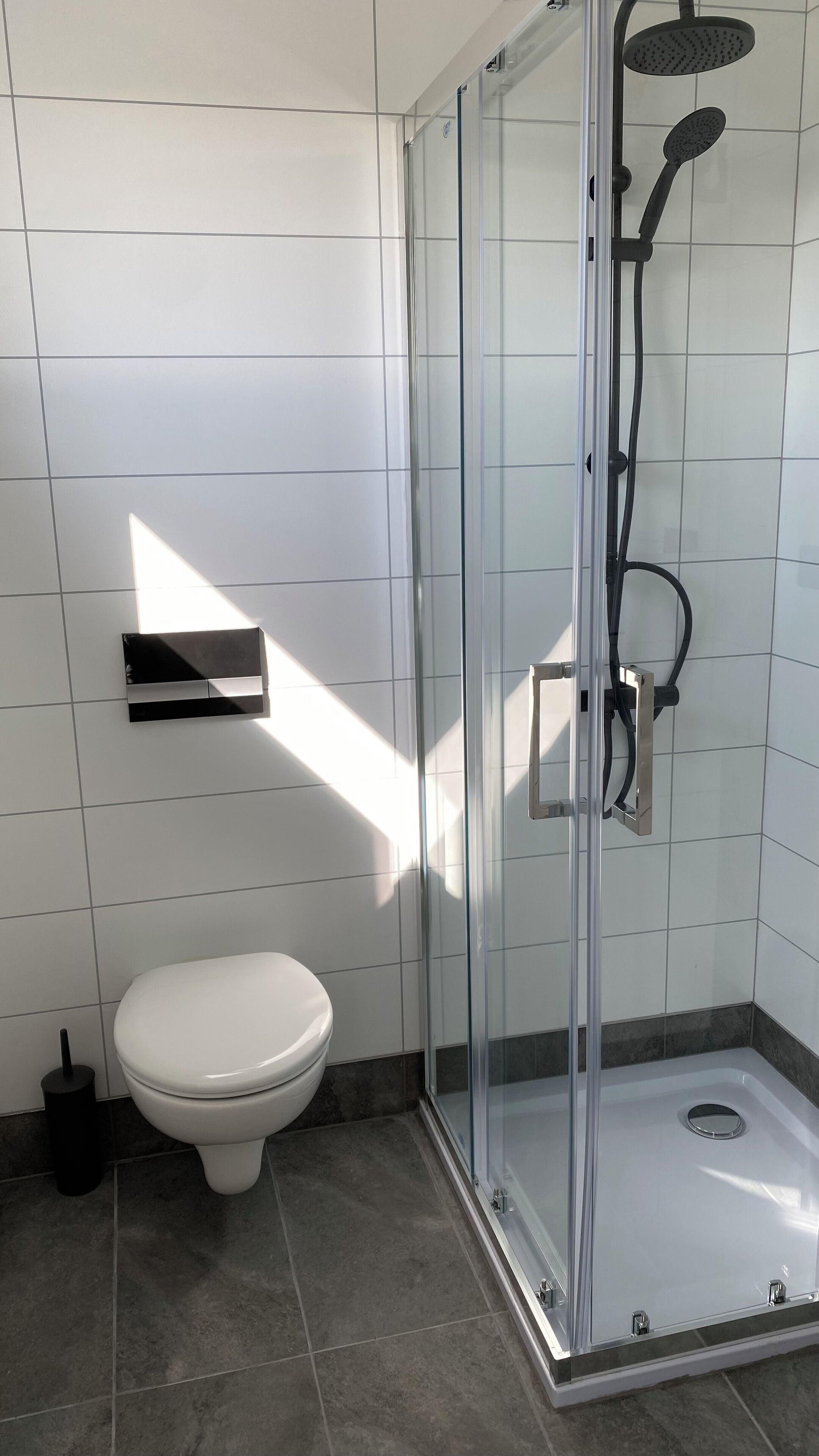 Een moderne badkamer met een douche met glazen wand, een wit toilet en een klein plankje.
