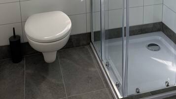 Een moderne badkamer met een douche met glazen wand, een wit toilet en een klein plankje.