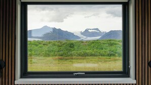Una ventana con vistas a un paisaje montañoso, incluyendo picos nevados y un primer plano con hierba.