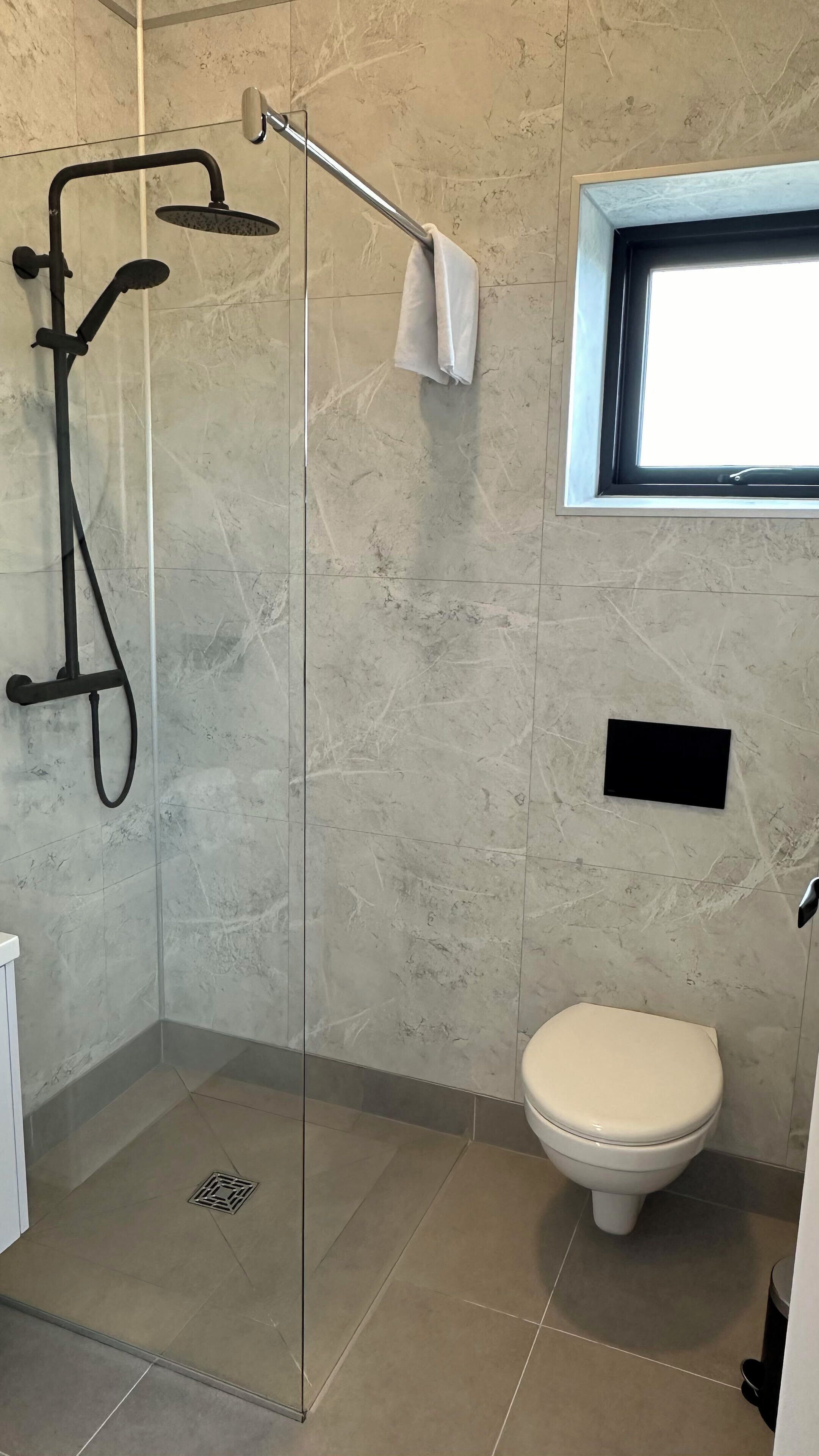 A bathroom with a glass-enclosed shower, a toilet, and a window.
