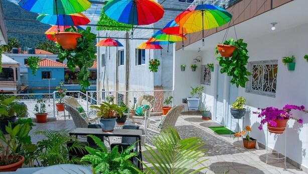 En tagterrasse med hængende plantekasser, udendørs møbler og udsigt til omkringliggende bygninger.