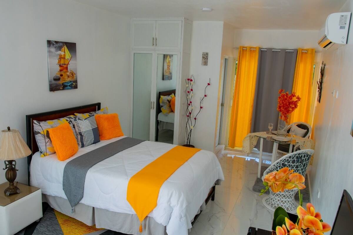 A hotel room with a bed, a nightstand, a desk, a chair, and a dining table with chairs.