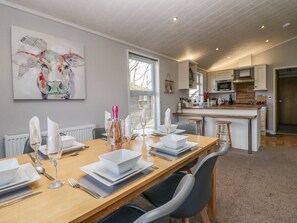 Een moderne keuken met een centraal eiland, een eethoek met een houten tafel gedekt voor een maaltijd, en een groot abstract schilderij aan de muur.