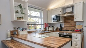 A modern kitchen with wooden countertops, white cabinets, and a built-in island with bar stools. - Lakeside 20 (Carnforth)