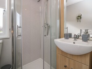 Een moderne badkamer met een glazen douchecabine, een witte wastafel met een houten kastje, en een kleine potplant aan de muur.