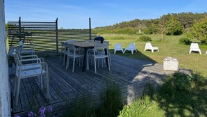 An outdoor patio with a wooden deck, white plastic chairs, and a barbecue grill. - Sodra Gotland 14 bed With Pool (Havdhem)