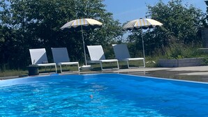 A swimming pool with clear blue water, surrounded by white lounge chairs and striped umbrellas. - Sodra Gotland 14 bed With Pool (Havdhem)