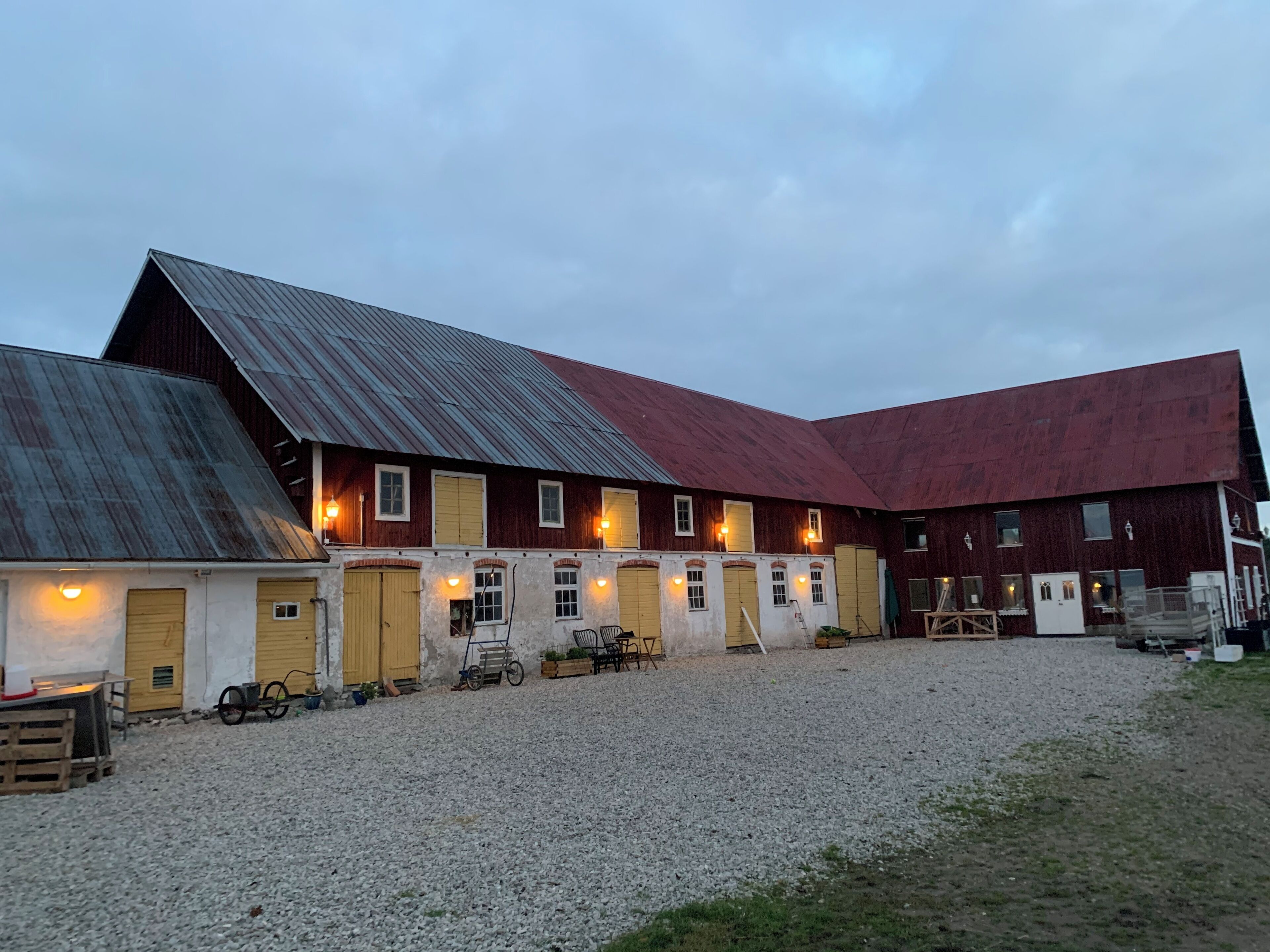 A large, multi-story barn with multiple doors and windows, a gravel driveway, and outdoor seating.