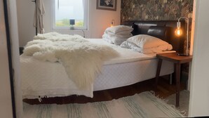 A bedroom with a bed, a window, a lamp, and a wall with a floral pattern. - Sodra Gotland 14 bed With Pool (Havdhem)