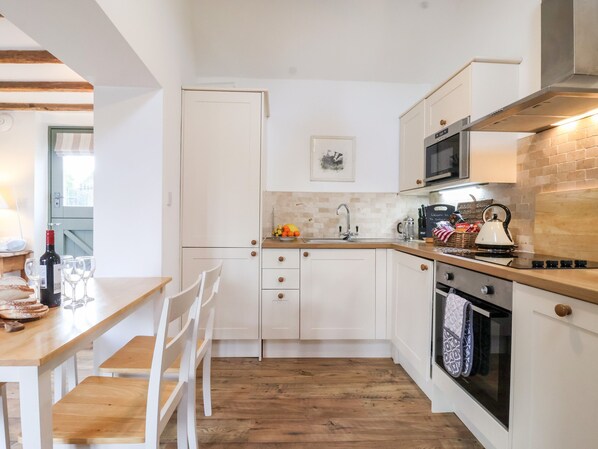 Une cuisine compacte avec des meubles blancs, un plan de travail en bois, un four à micro-ondes, une bouilloire et un évier.
