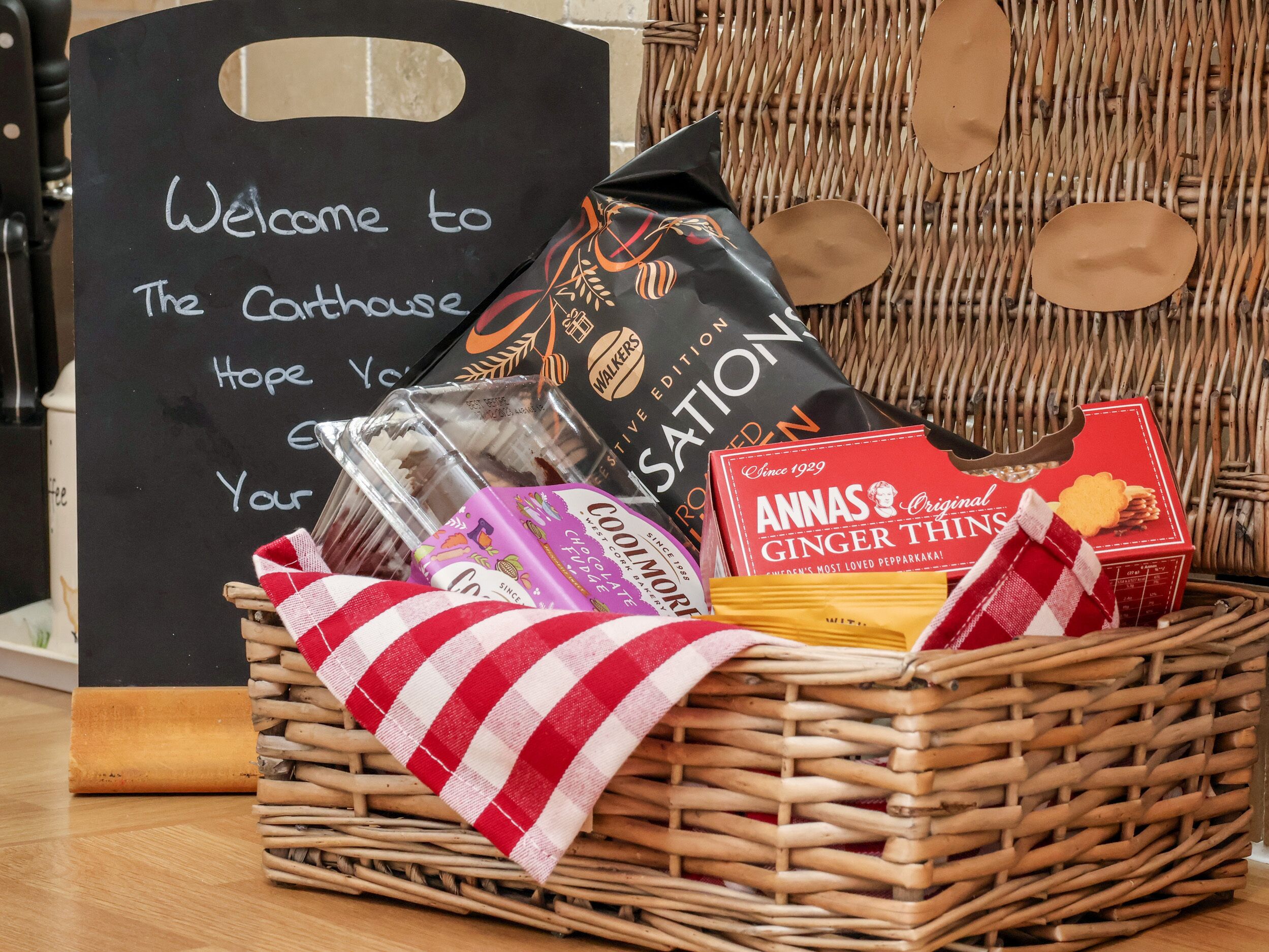 A wicker basket filled with various food items and a sign that reads "Welcome to The Carthouse Hope You Enjoy Your Stay".