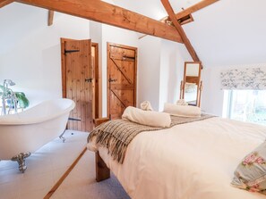 Une chambre à coucher avec un grand lit, un plafond en bois, une baignoire et une porte au design inspiré des portes de grange.